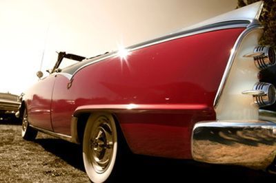 A red and white classic car is parked in the dirt.