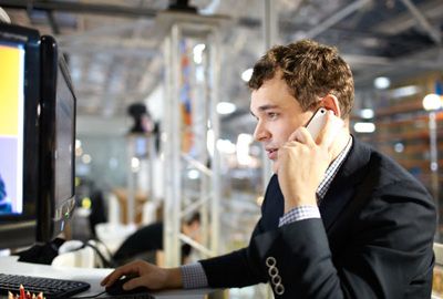 A man in a suit is talking on a cell phone while using a computer.