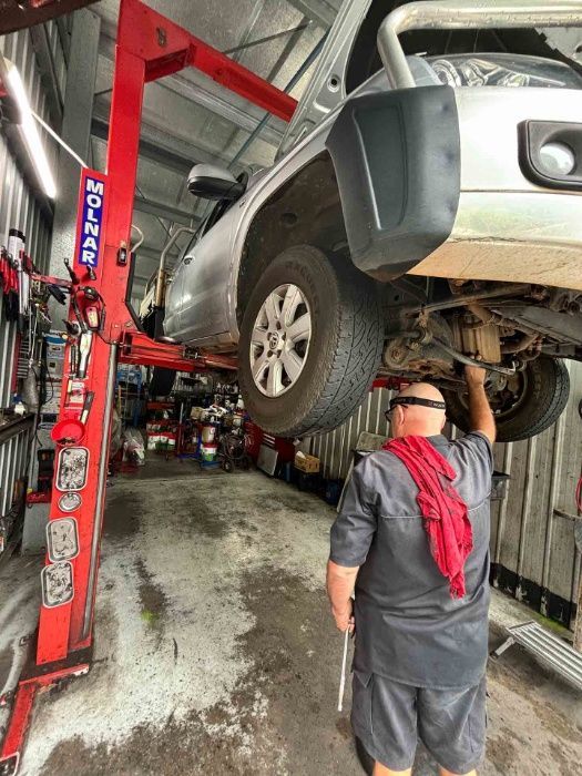 A Man Is Working On The Underside Of A Car In A Garage — Master Mechanix In Yandina Creek, QLD