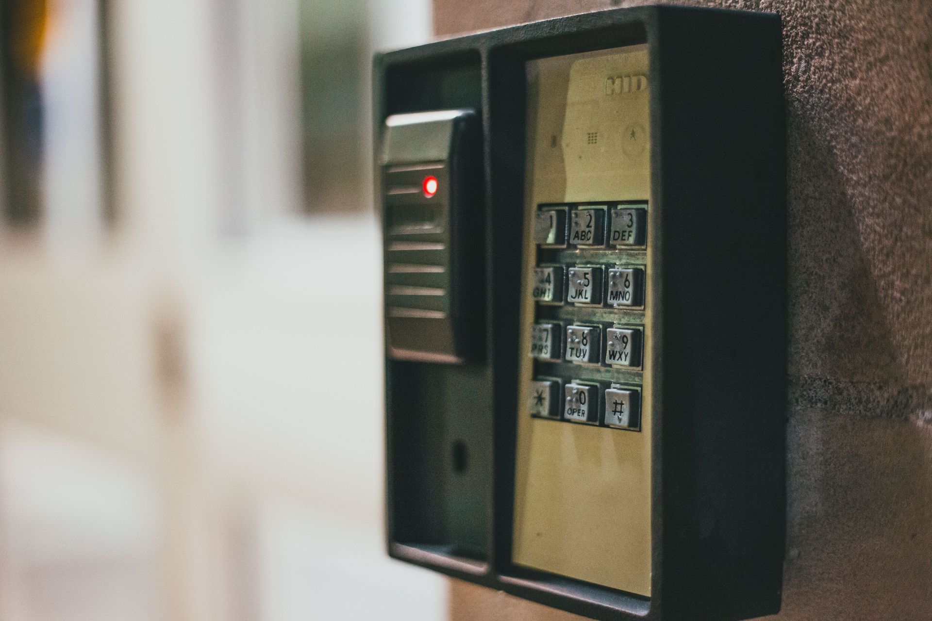 Close-up of a wall-mounted keypad door intercom with a lit red indicator light