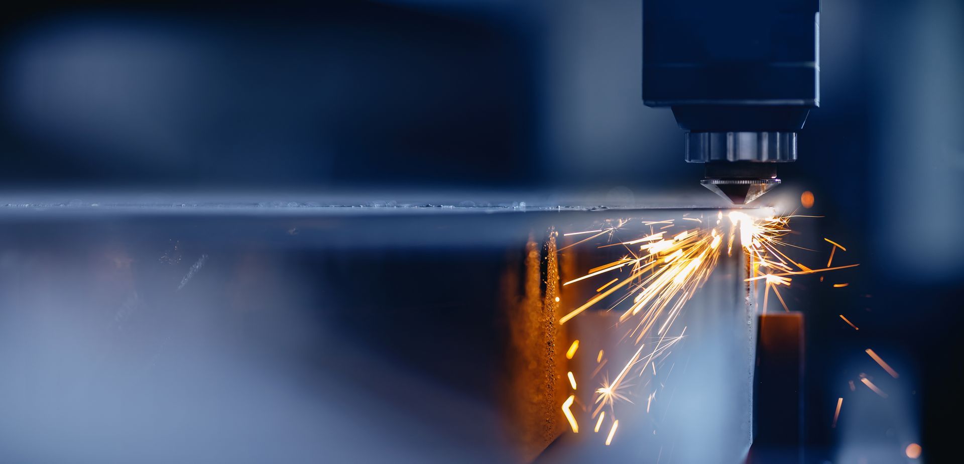 Close view of a metal sheet being cot by a laser cutter, with sparks flying.