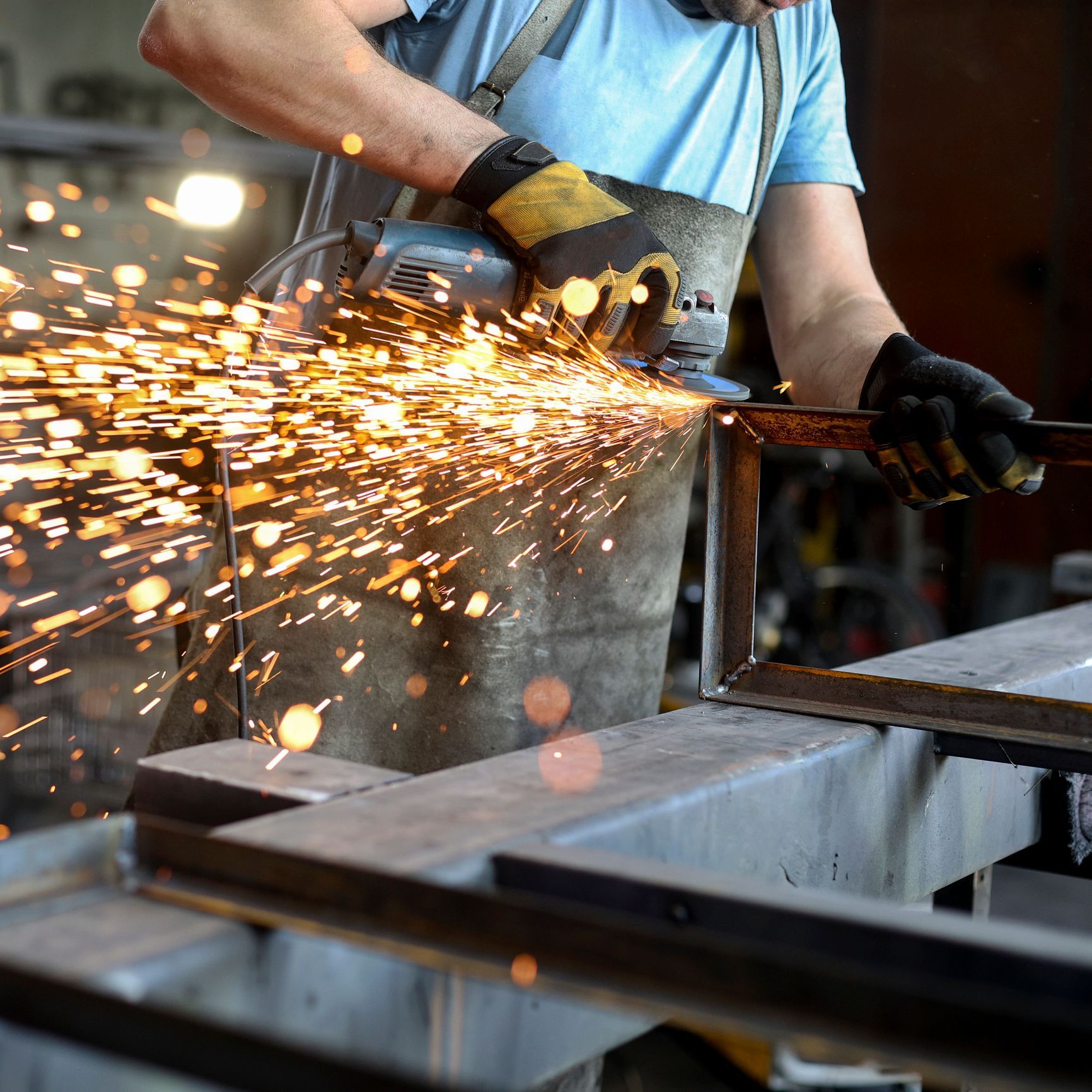 A worker cutting metal with an angle grinder in a workshop and bright sparks flying