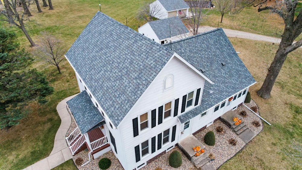 Aerial view of a white house with a dark roof, black shutters, and a landscaped front yard in autumn.