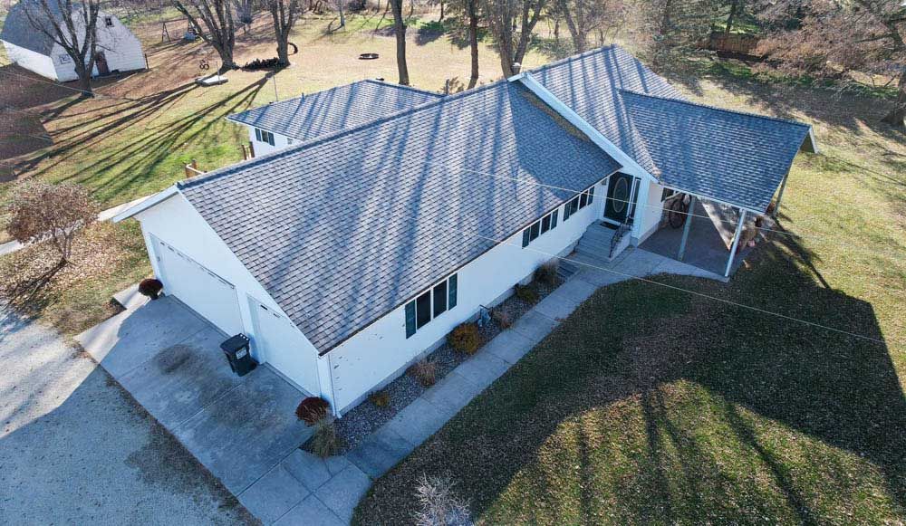 Aerial view of a white house with a gray roof and a small covered porch, surrounded by grass and trees.