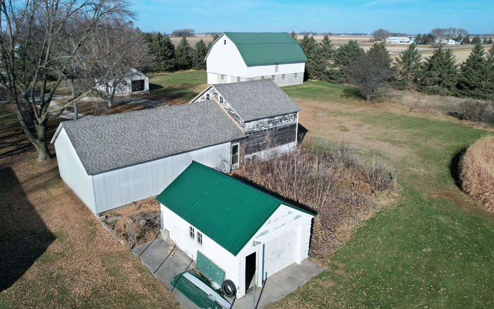 Aerial view of a rural farmyard with white barns, a green-roofed shed, and open grassy fields.