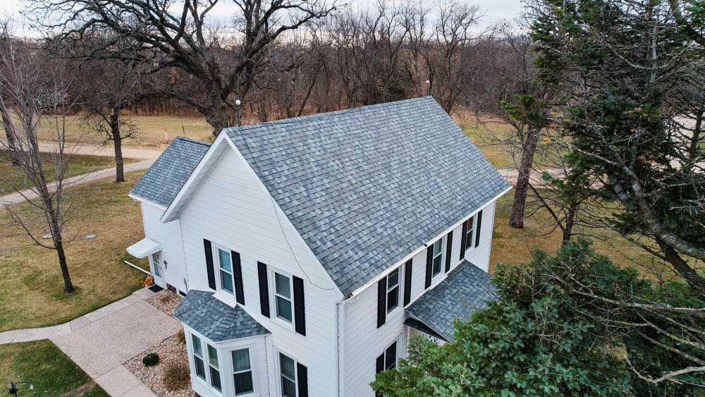 Aerial view of a white two-story house with a gray roof, surrounded by leafless trees and lawn.