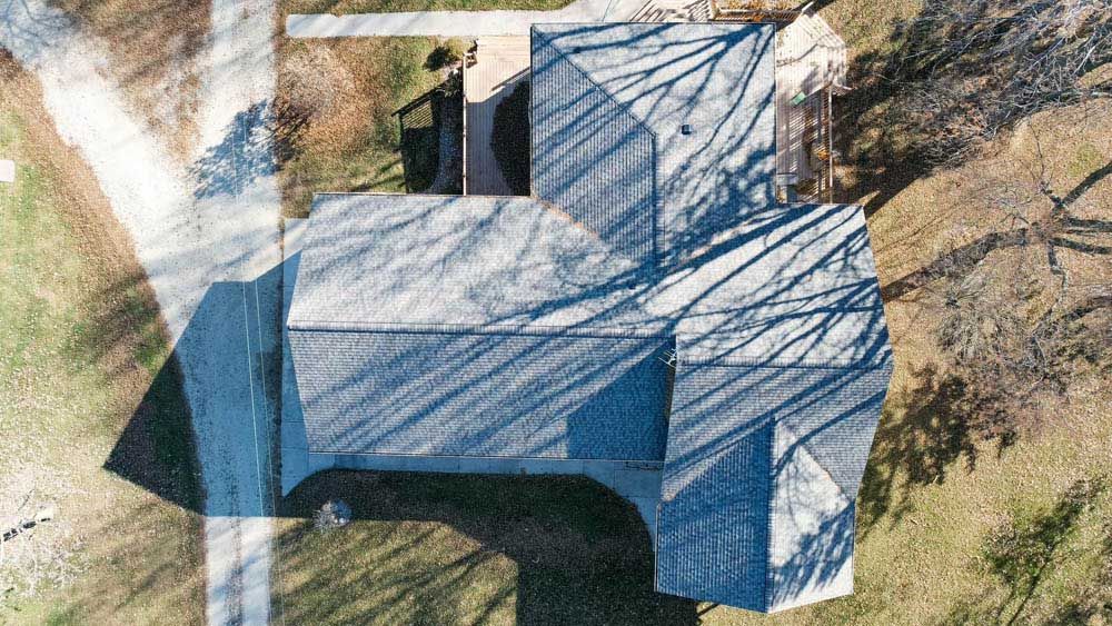 Aerial view of a blue-roofed house with surrounding trees and grass.