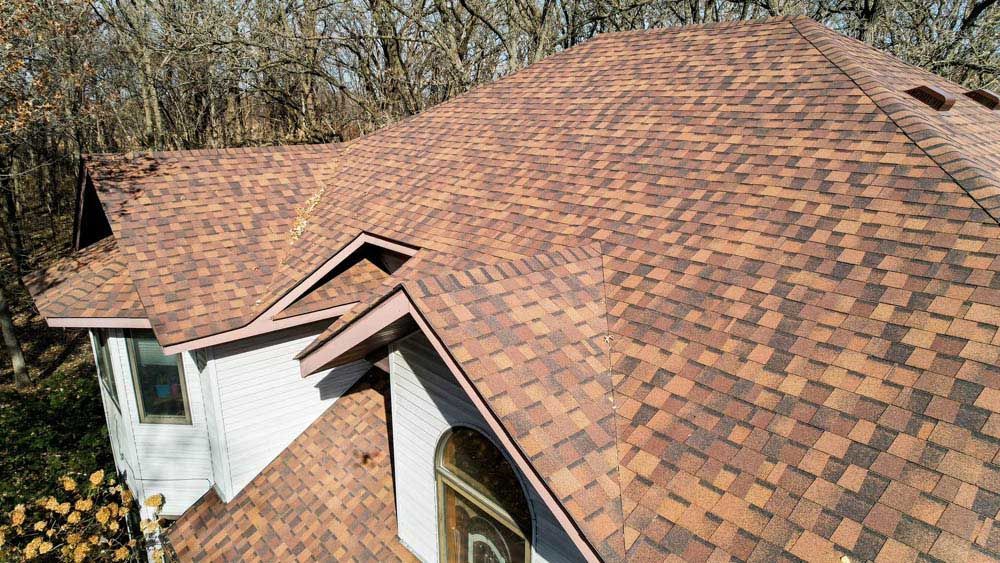 Brown shingle roof on a house with trees in the background