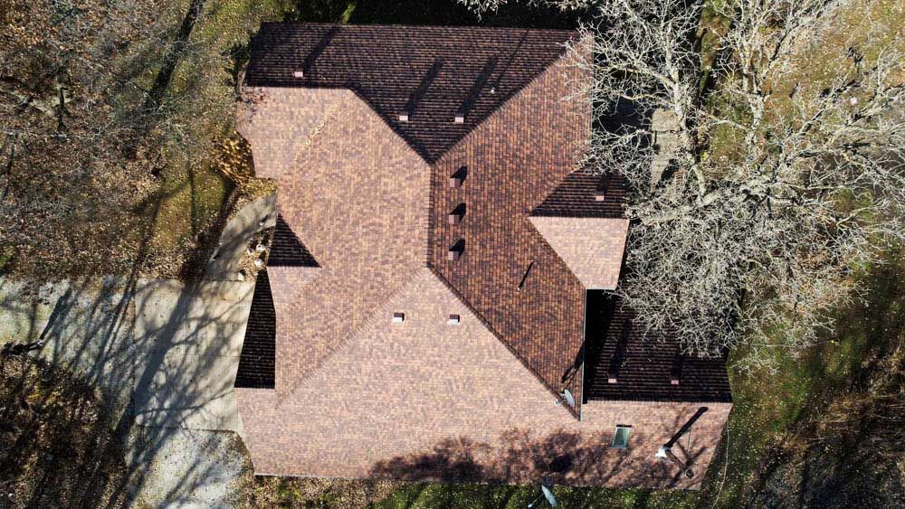 Aerial view of a tan shingle-roof house surrounded by trees and foliage.