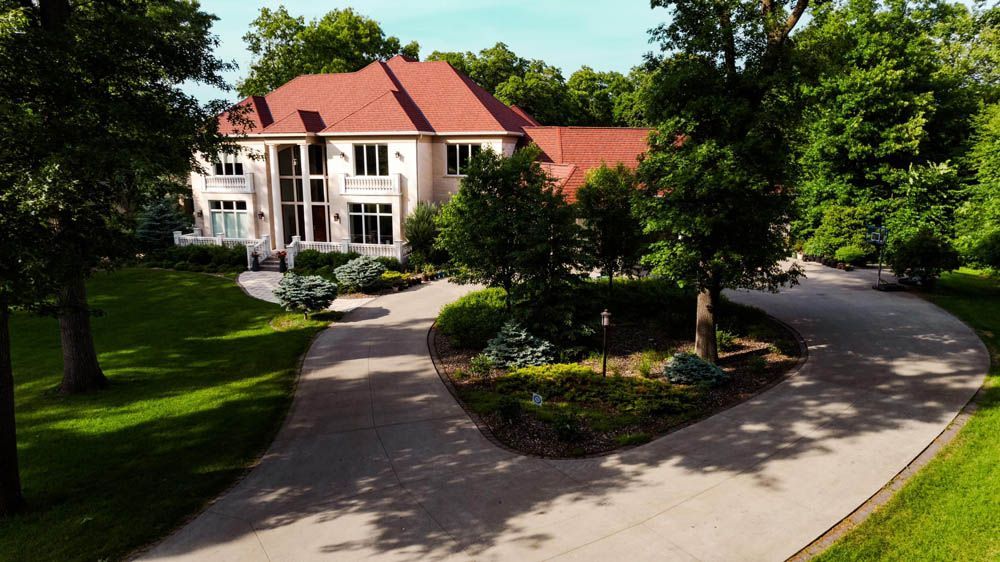 Large white house with a red roof, viewed from a curved driveway surrounded by trees and lawn.