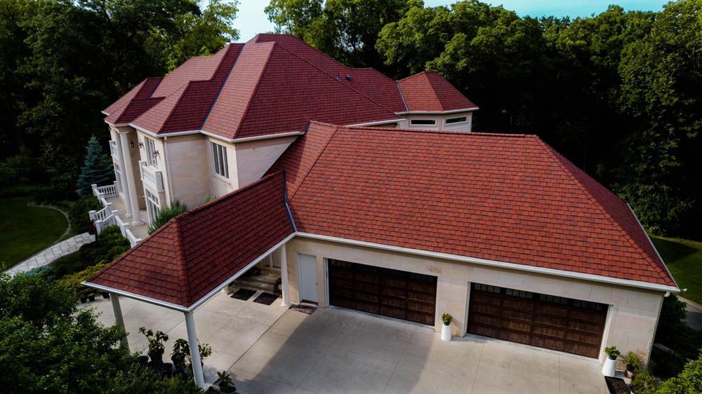 Aerial view of a large house with red roofs, cream walls, and a three-car garage surrounded by trees