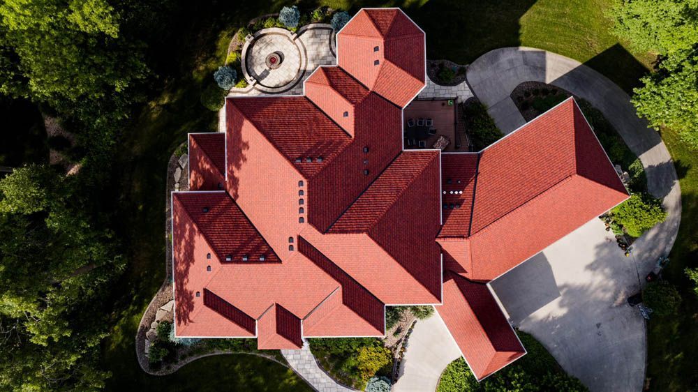 Aerial view of a red-roofed house surrounded by trees and a curved driveway.
