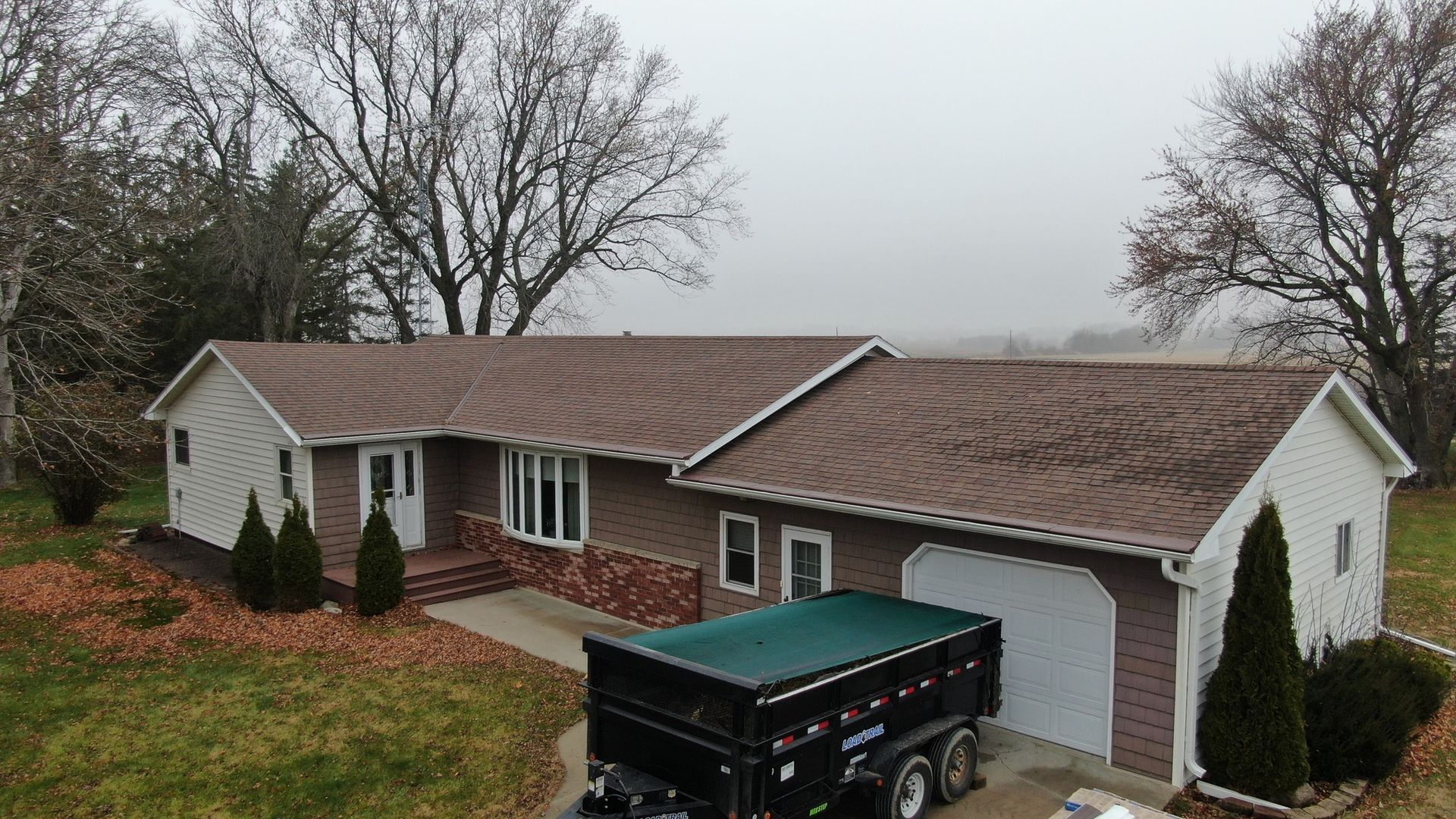 Suburban house with gray siding, brown roof, and a black SUV parked in the driveway on a foggy day
