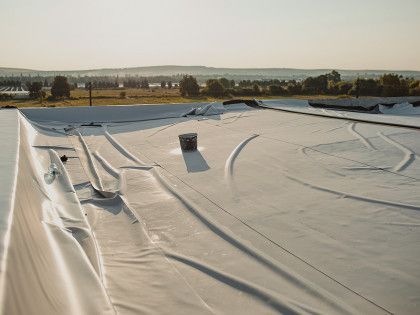 White tarp-covered flat roof with folds and a small vent, overlooking fields at sunset