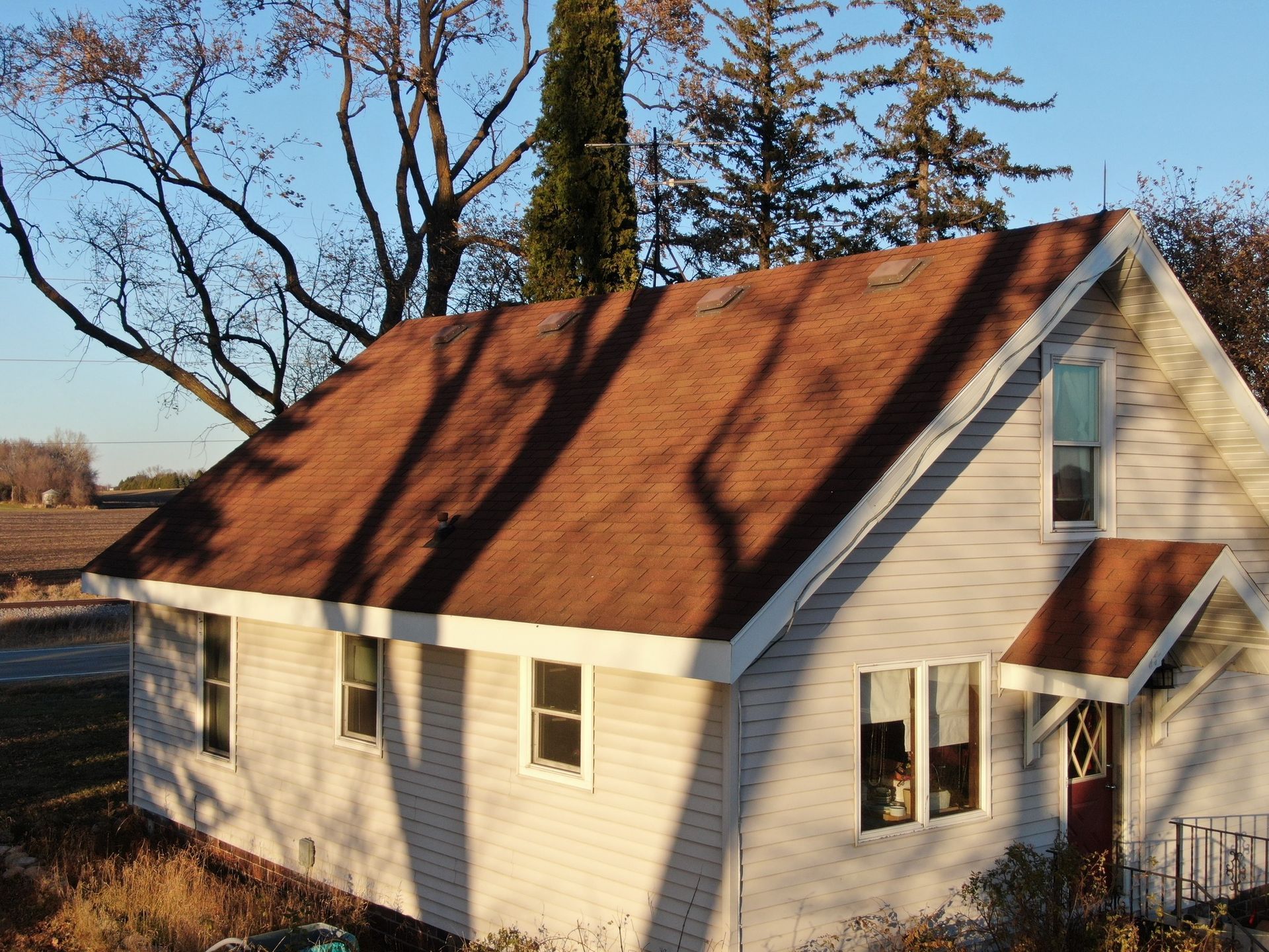 White house with red roof and tall trees in warm sunlight