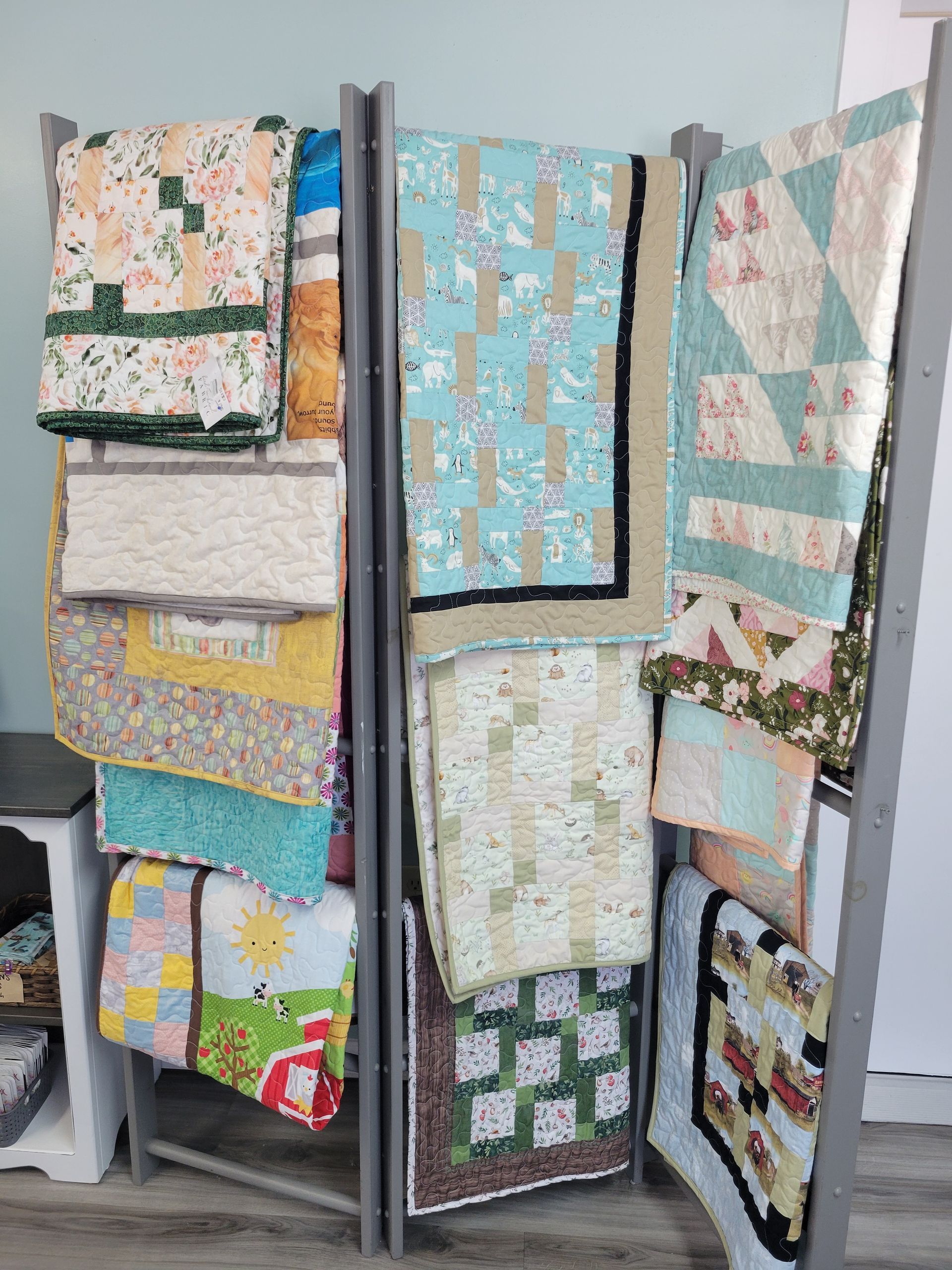 Colorful quilted blankets and fabrics draped over a metal rack indoors.