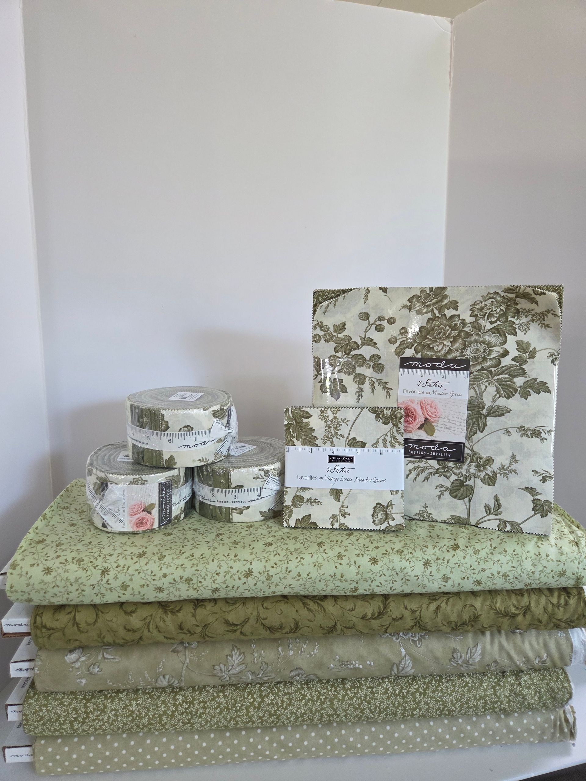 Stacked green floral fabrics with matching round containers and a framed floral print on top.