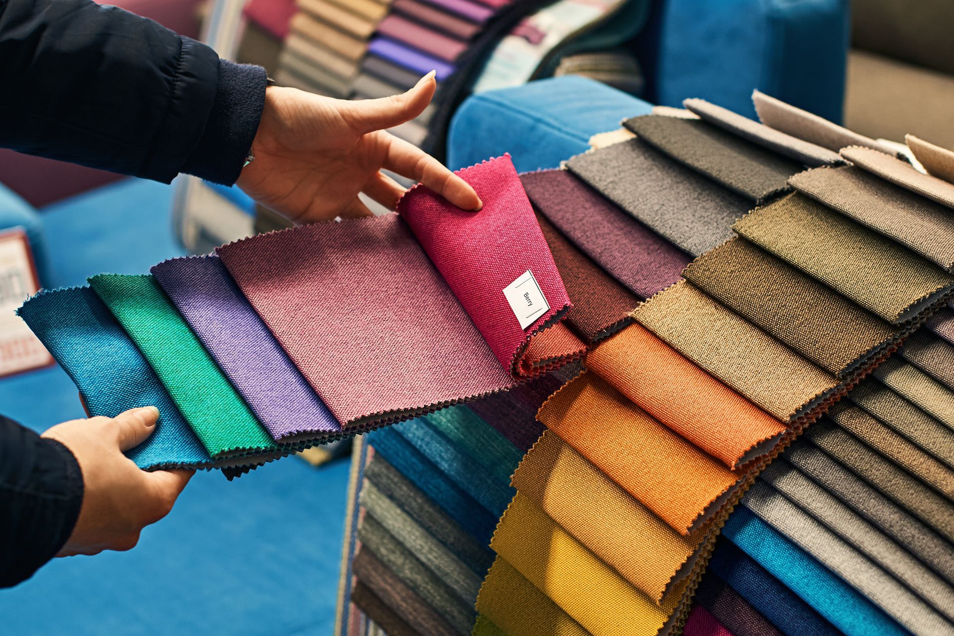 Hands holding a fan of colorful fabric swatches beside neatly stacked upholstery samples.