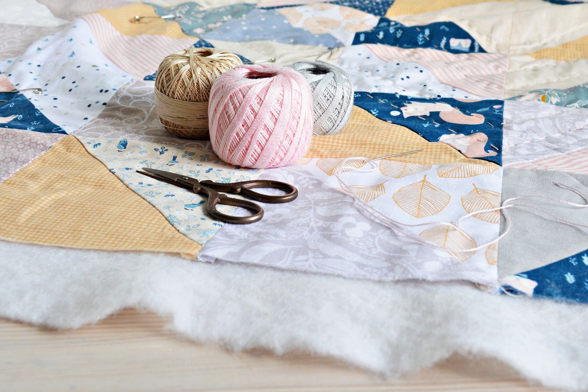 Quilting cotton fabric pieces with thread and sewing scissors.
