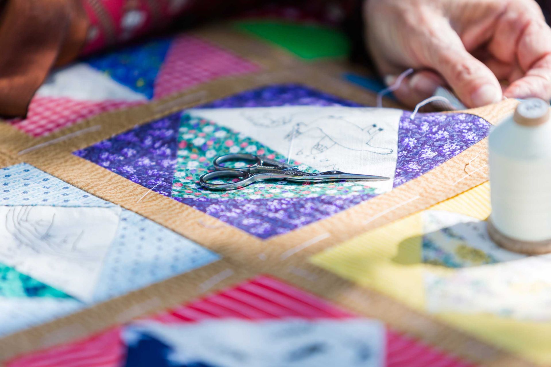 Colorful quilt blocks being hand stitched with scissors and thread nearby.