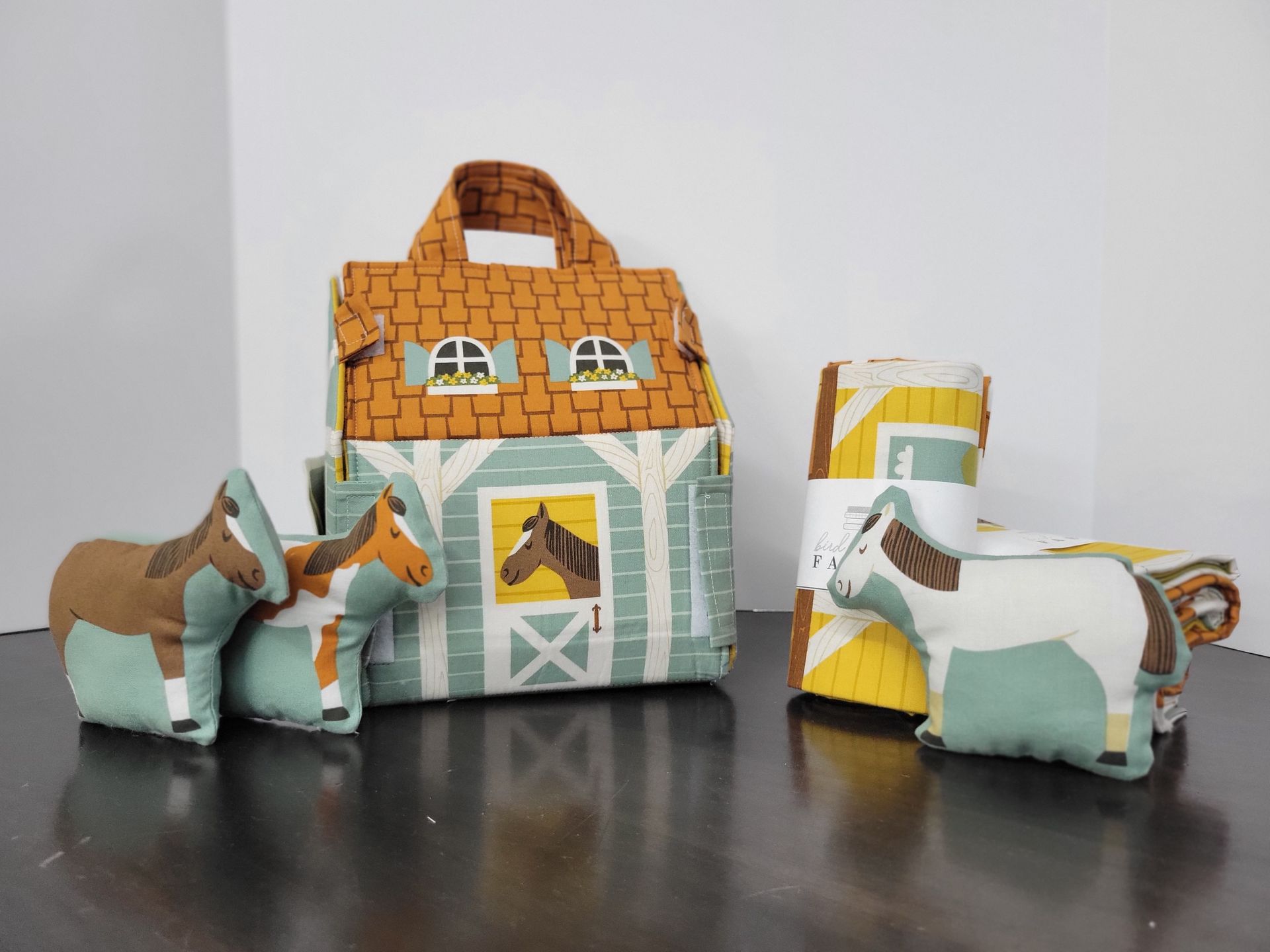 Paper toy horses beside a small paper house and cart on a tabletop