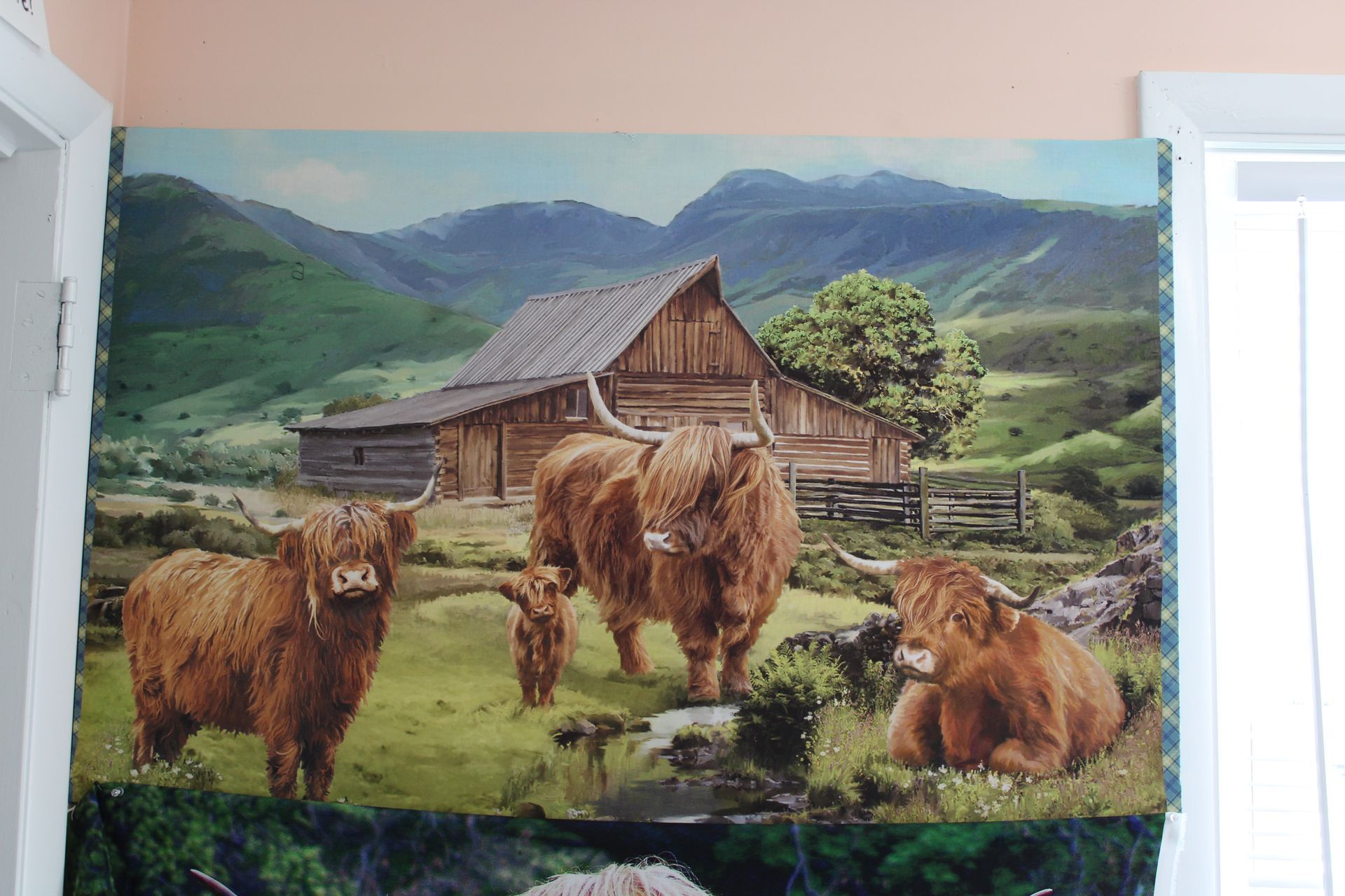 Three fluffy brown cattle in front of a rustic cabin with green mountains behind them