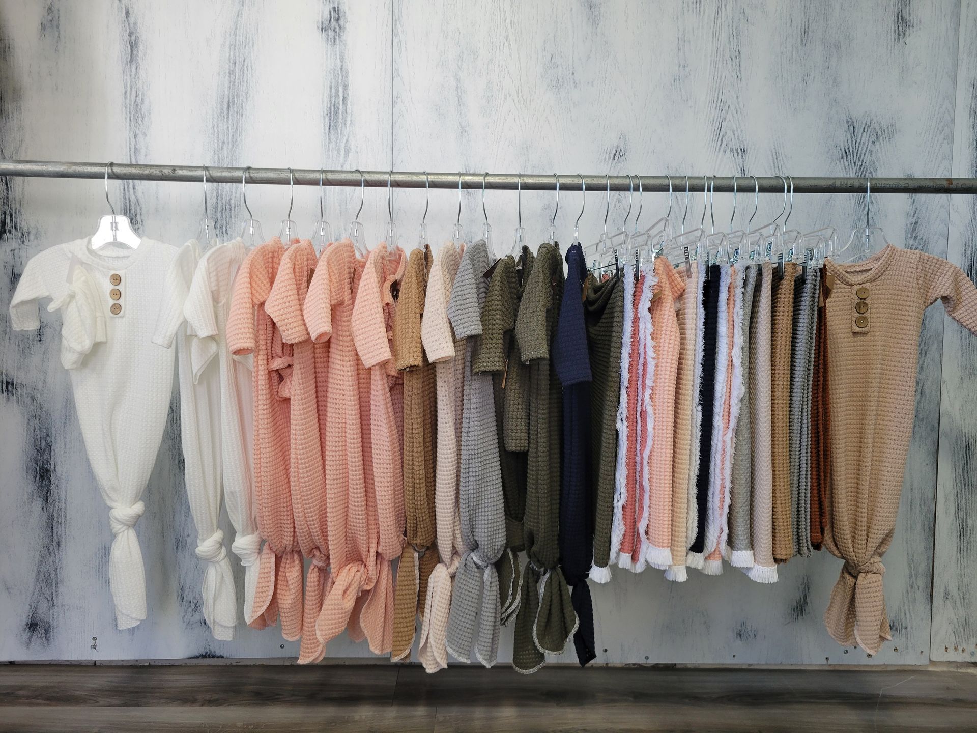 Children's clothes hanging on a rack against a white wall, in soft pink, beige, and white tones