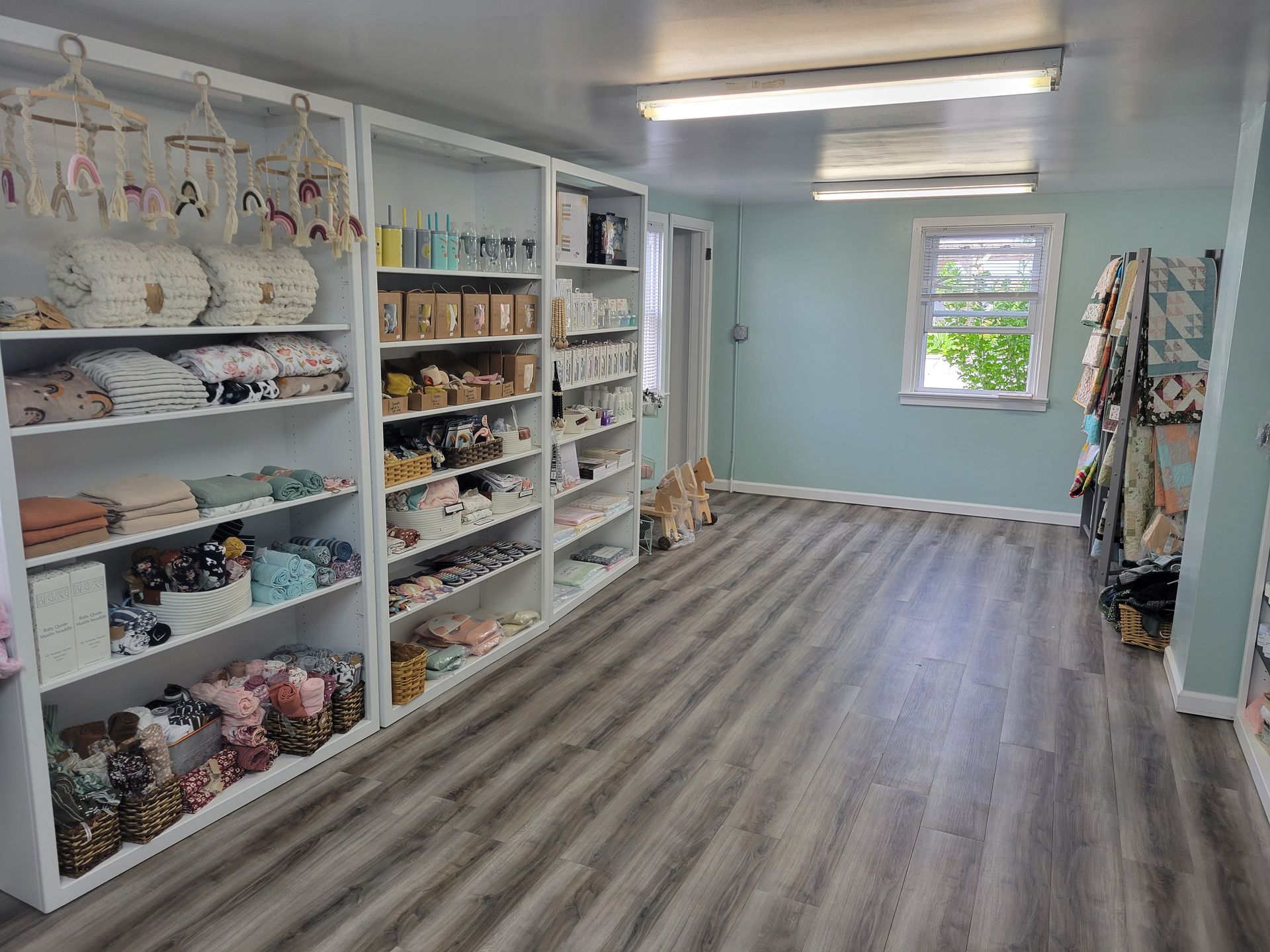 Bright fabric and craft shop aisle with shelves of supplies and garments, light blue walls, and wood-look flooring