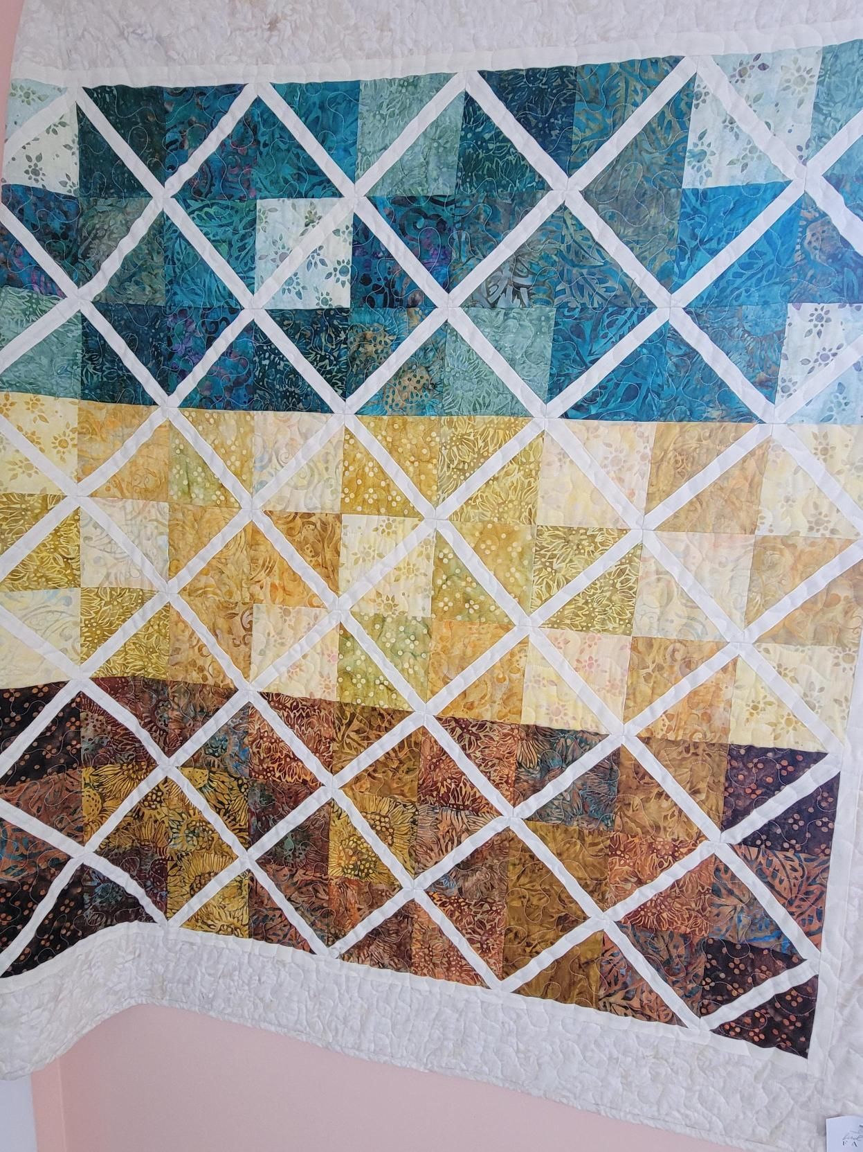 Colorful geometric quilt with white crisscross lines in blue, gold, and brown sections on a wall