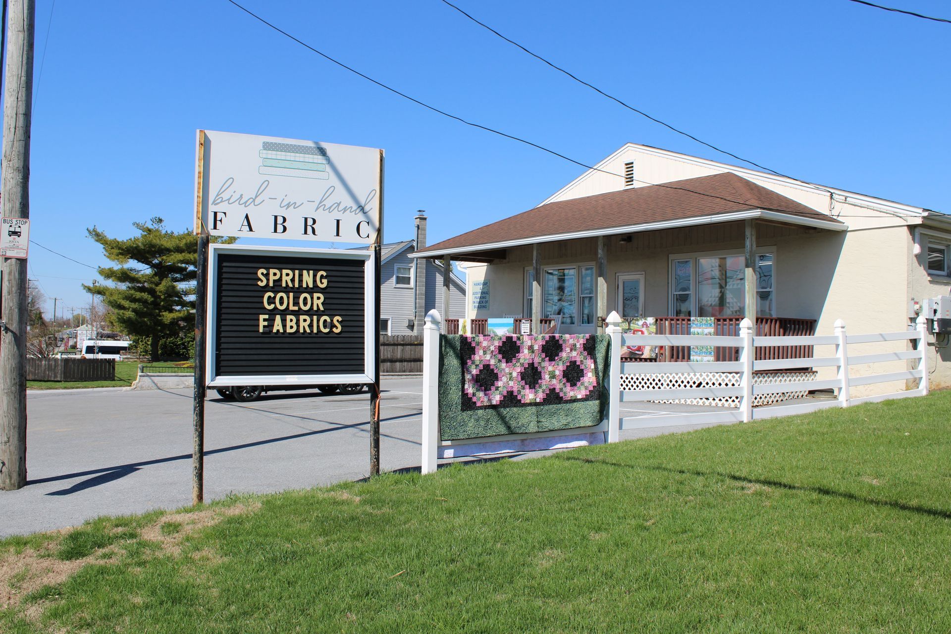 Spring Color Fabrics storefront with sign and small house, beside a grassy roadside.
