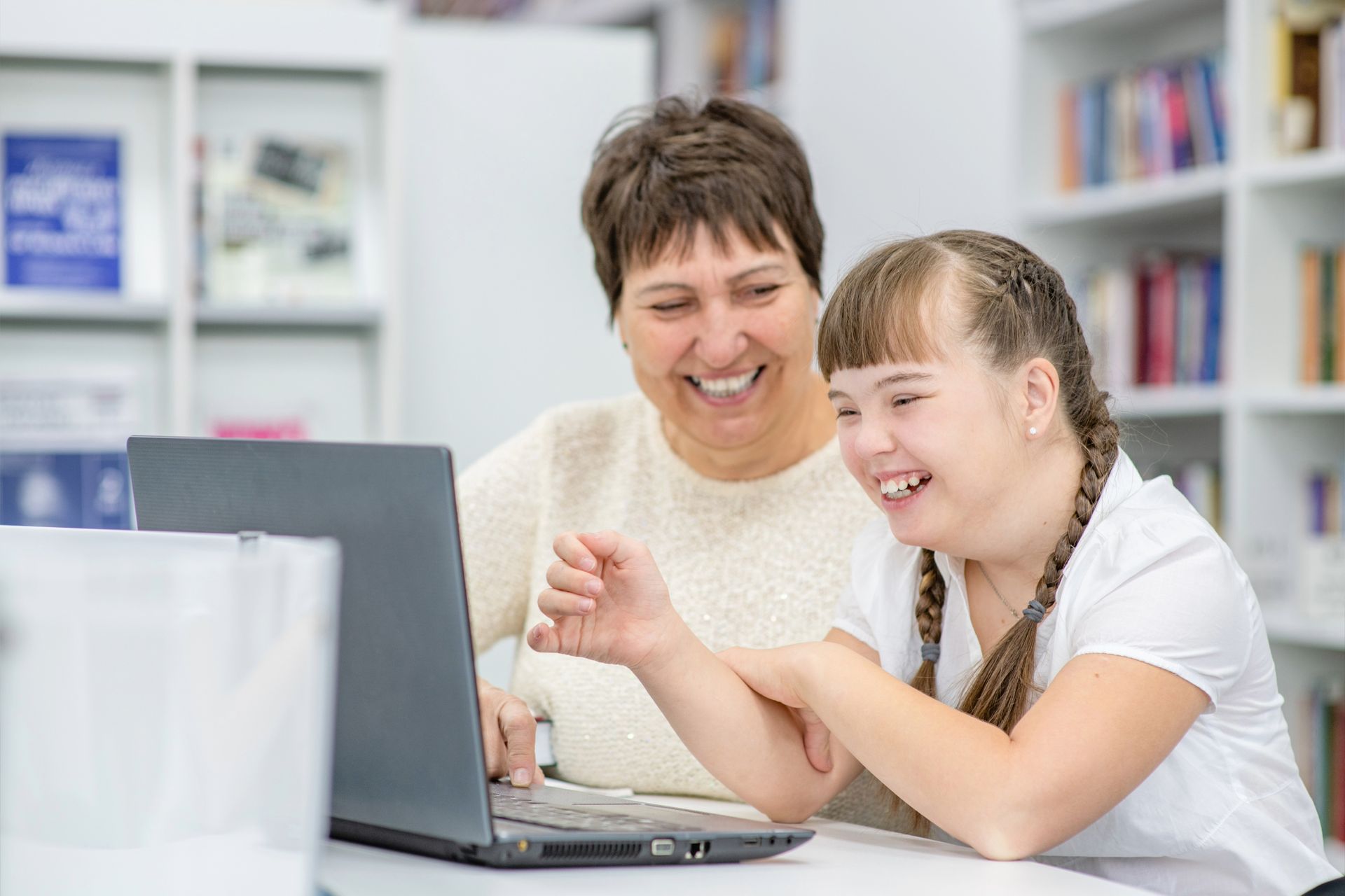A woman and a girl are looking at a tablet in a kitchen.