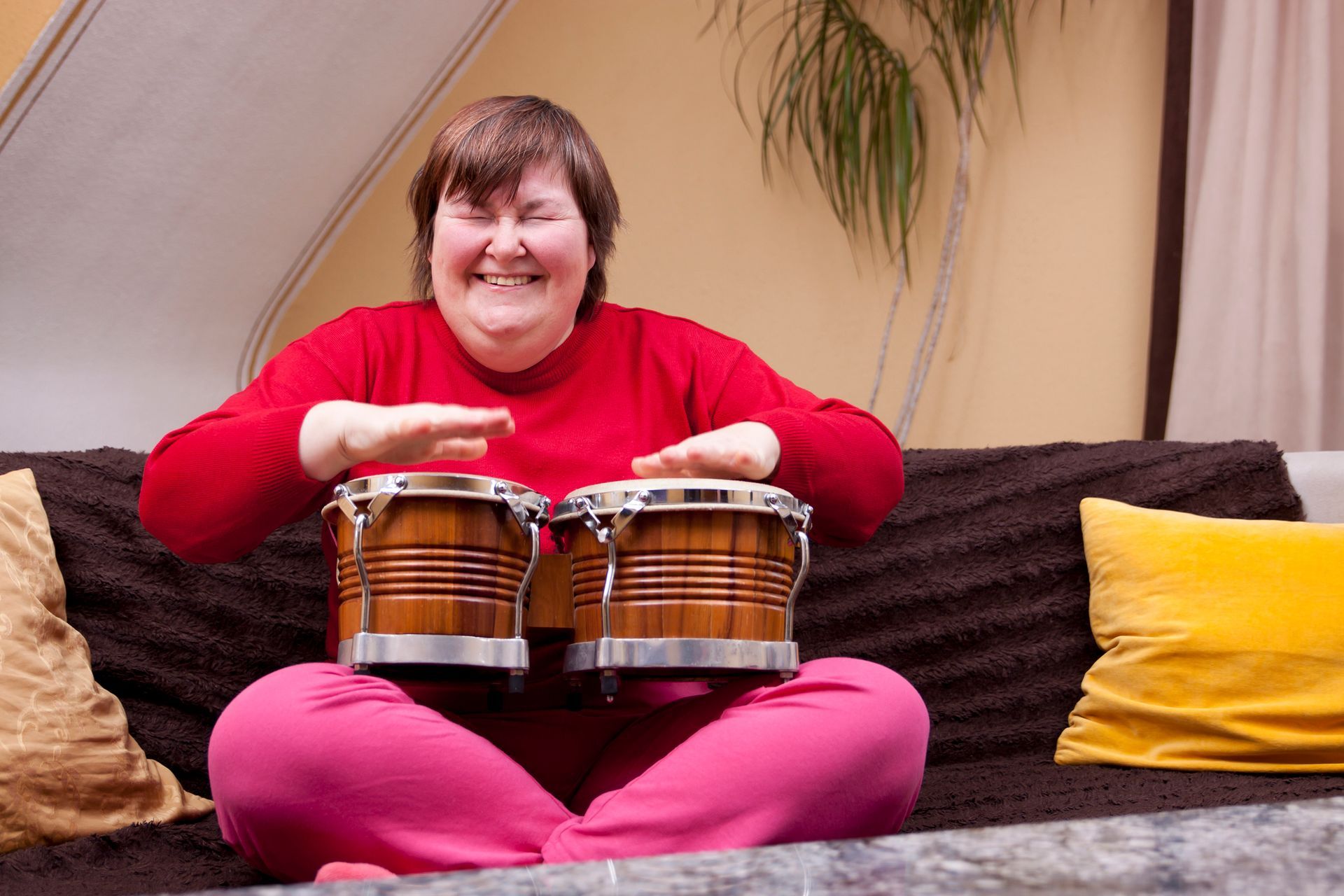 A woman is sitting on a couch holding two drums and smiling.