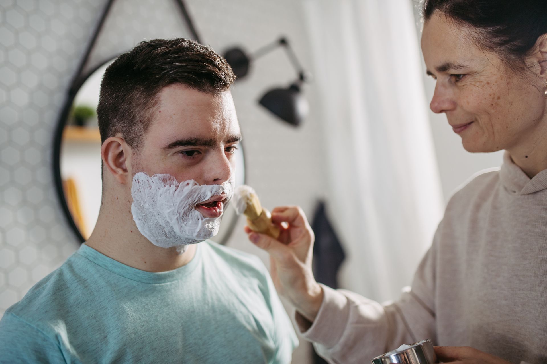Woman applying shaving cream to a man's face in a bathroom.