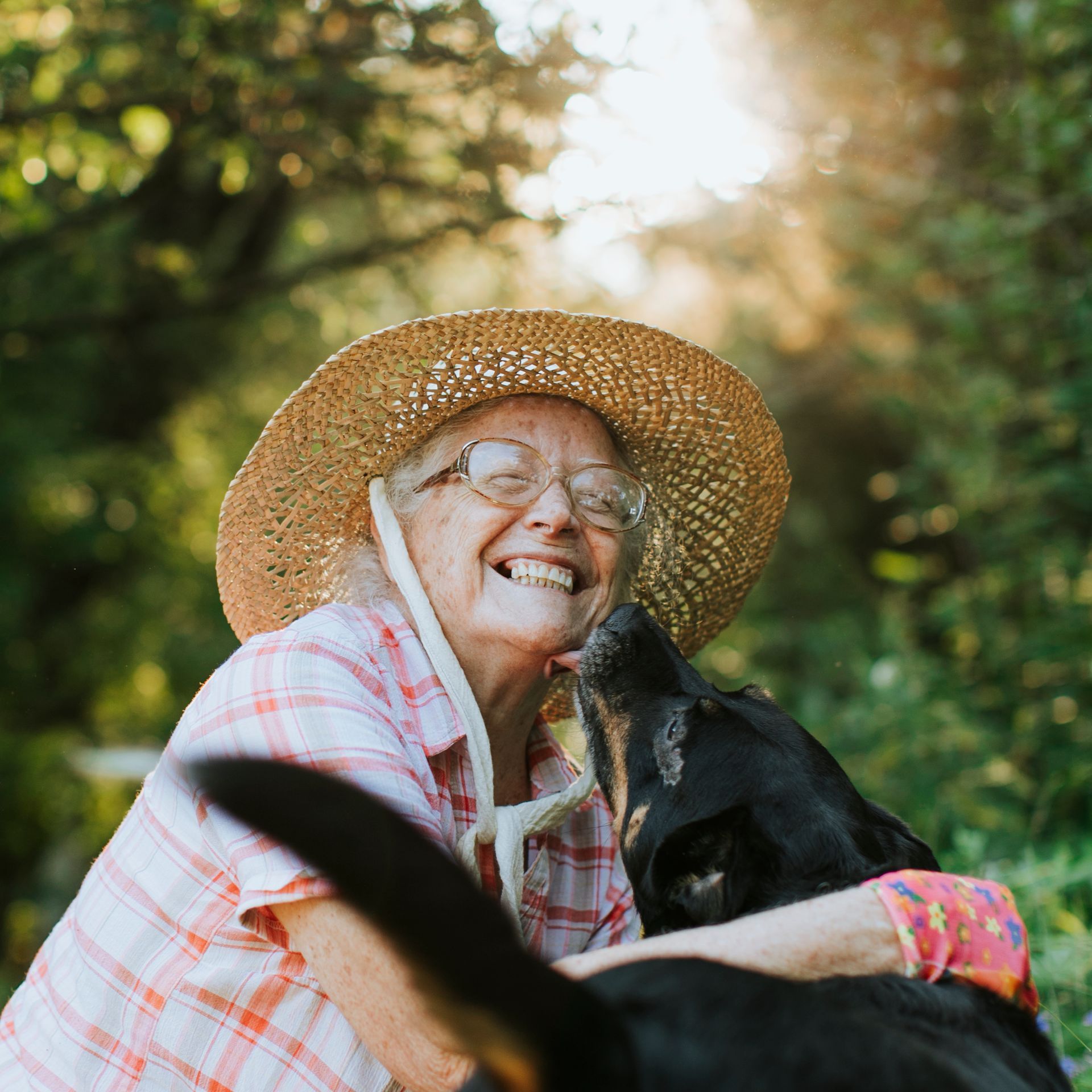 A woman wearing a straw hat is hugging a black dog