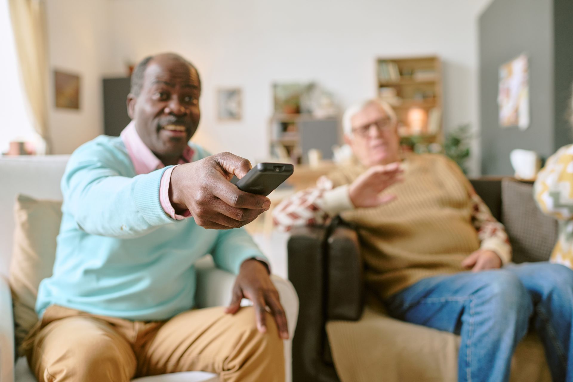 A man is holding a remote control while sitting on a couch next to another man.