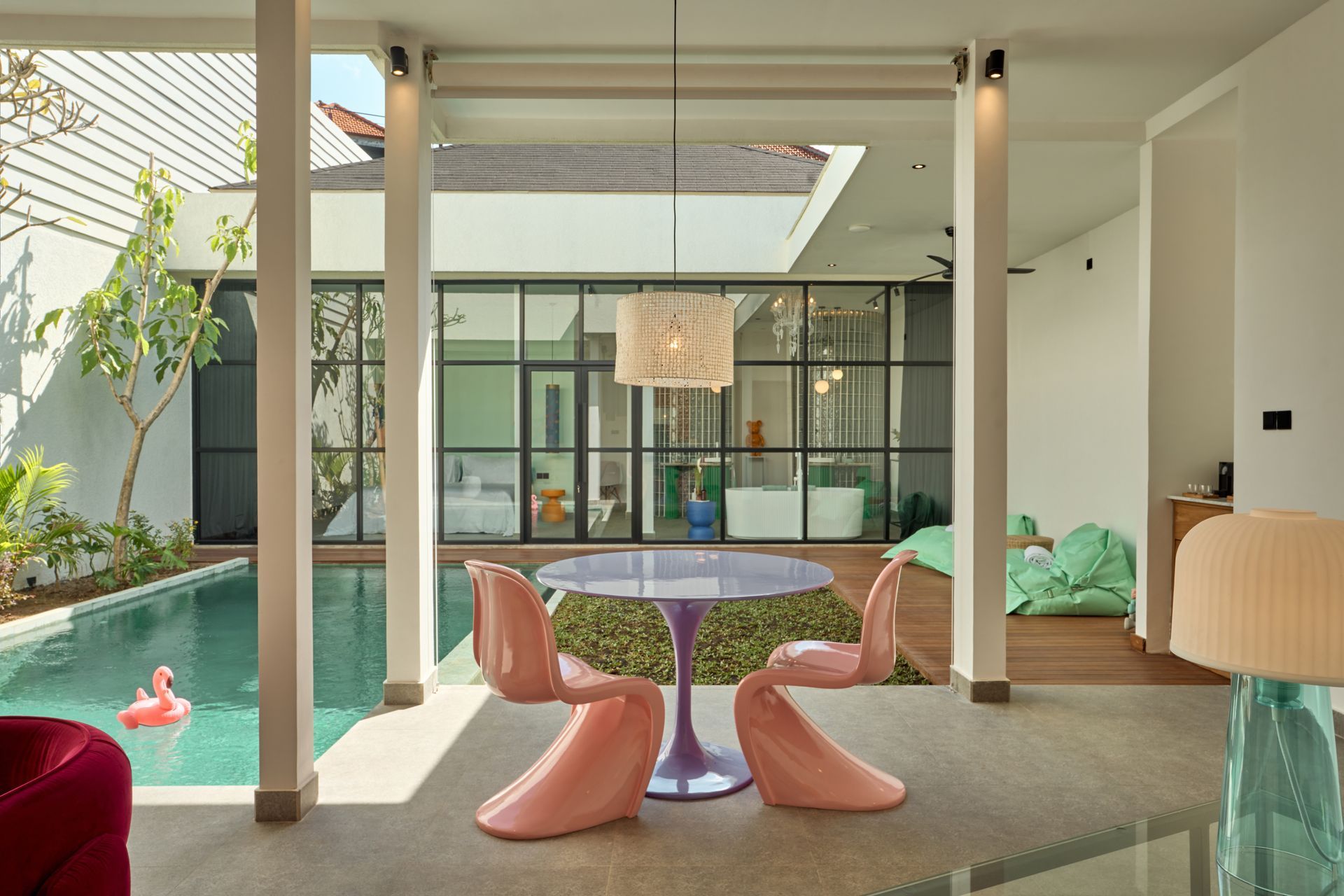 Modern patio with pink chairs, round table, pool, and open indoor-outdoor living space