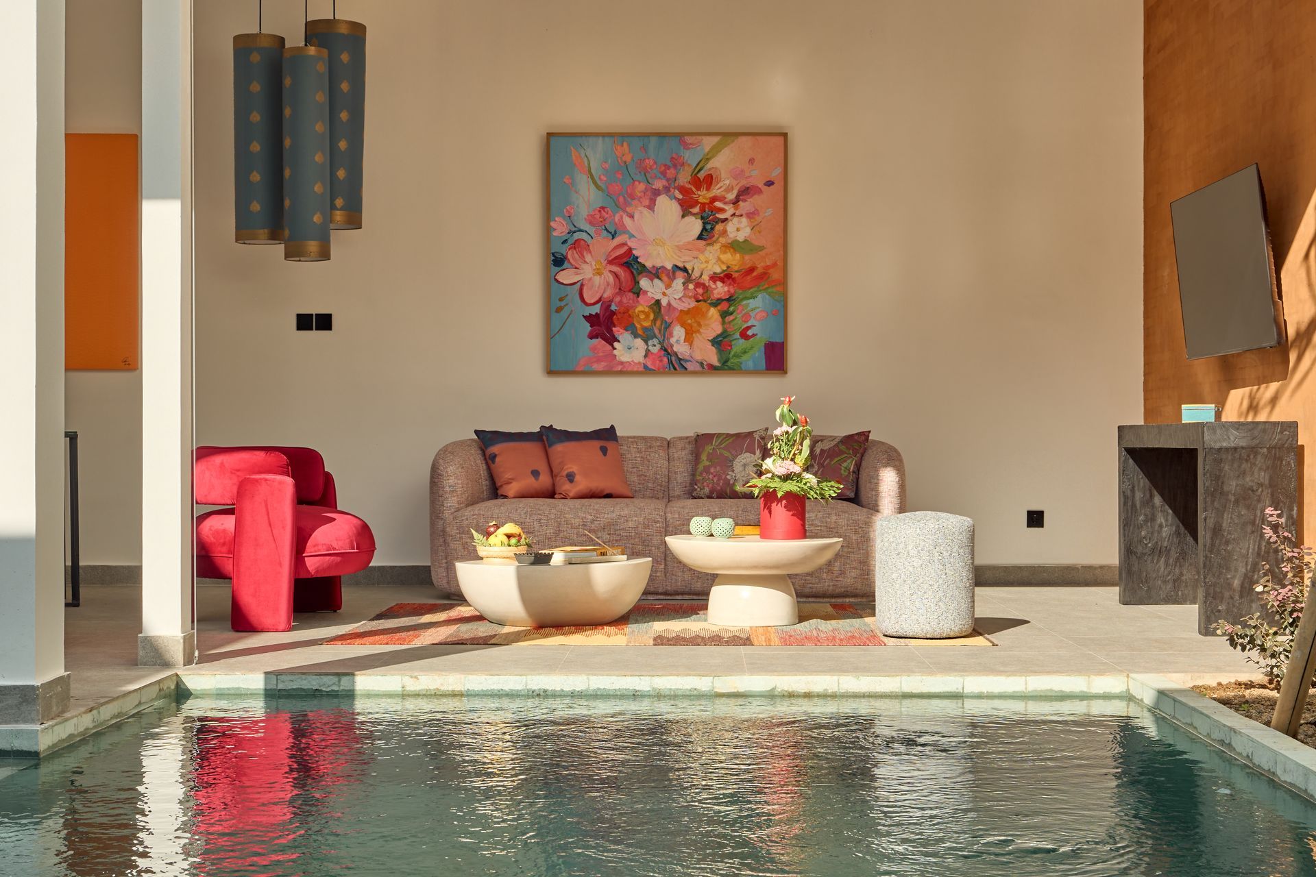 Modern poolside lounge with red chair, colorful wall art, and a turquoise swimming pool