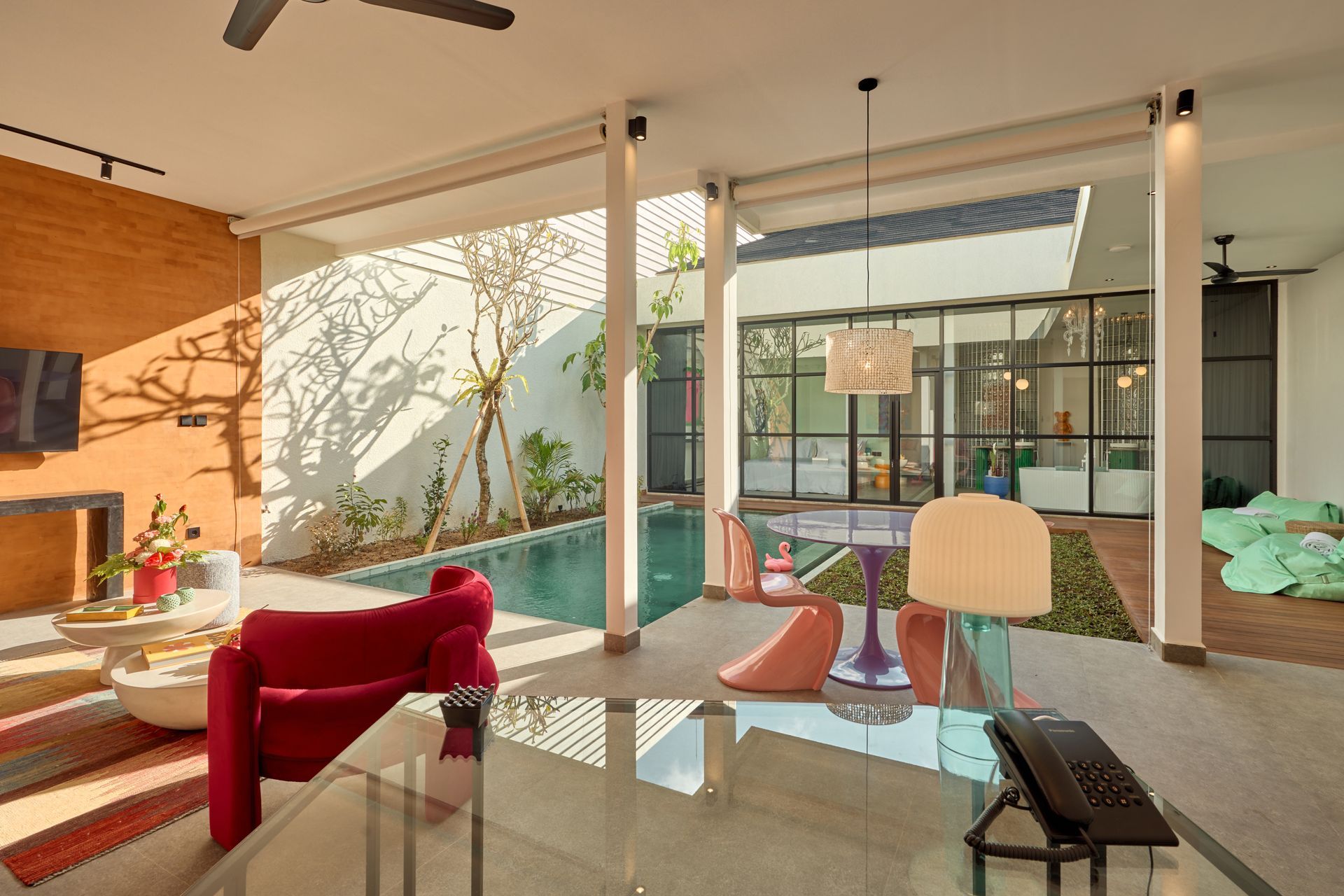 Modern living room with red chair, glass table, and open view to a sunlit patio and pool