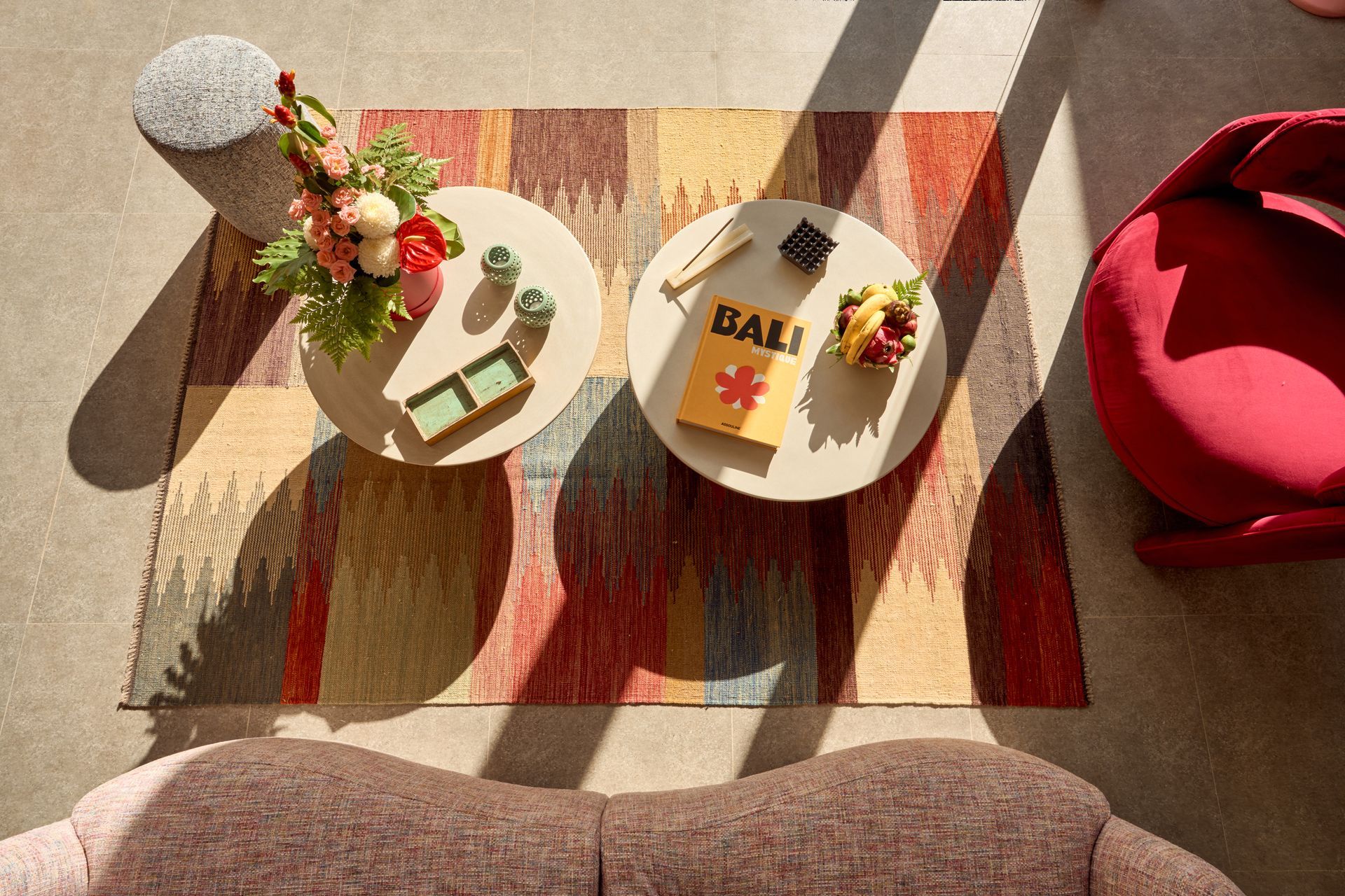 Top-down view of a cozy living room table with snacks, flowers, and a red chair on a patterned rug