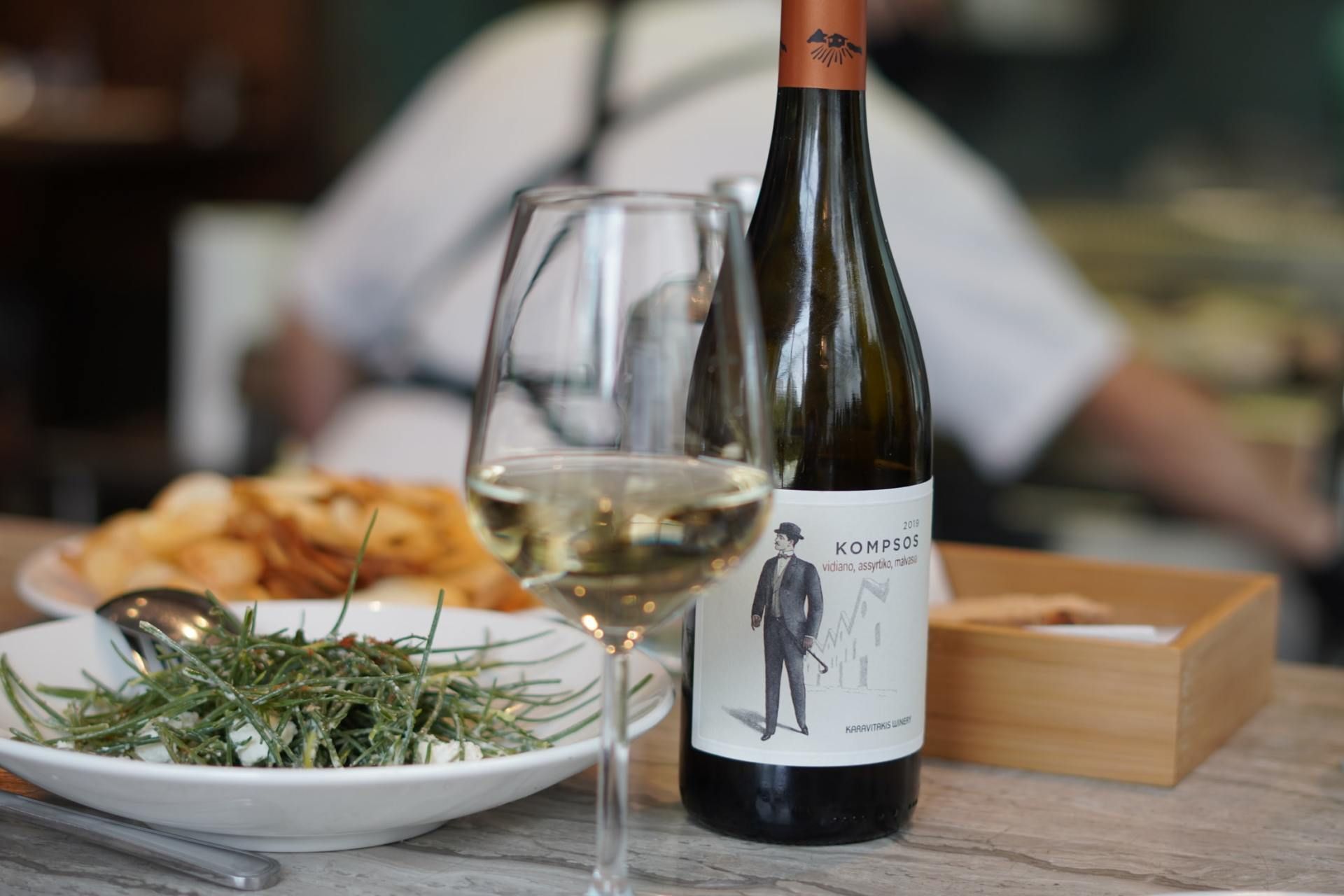 Wine bottle and glass on a table beside salad and bread in a casual dining setting