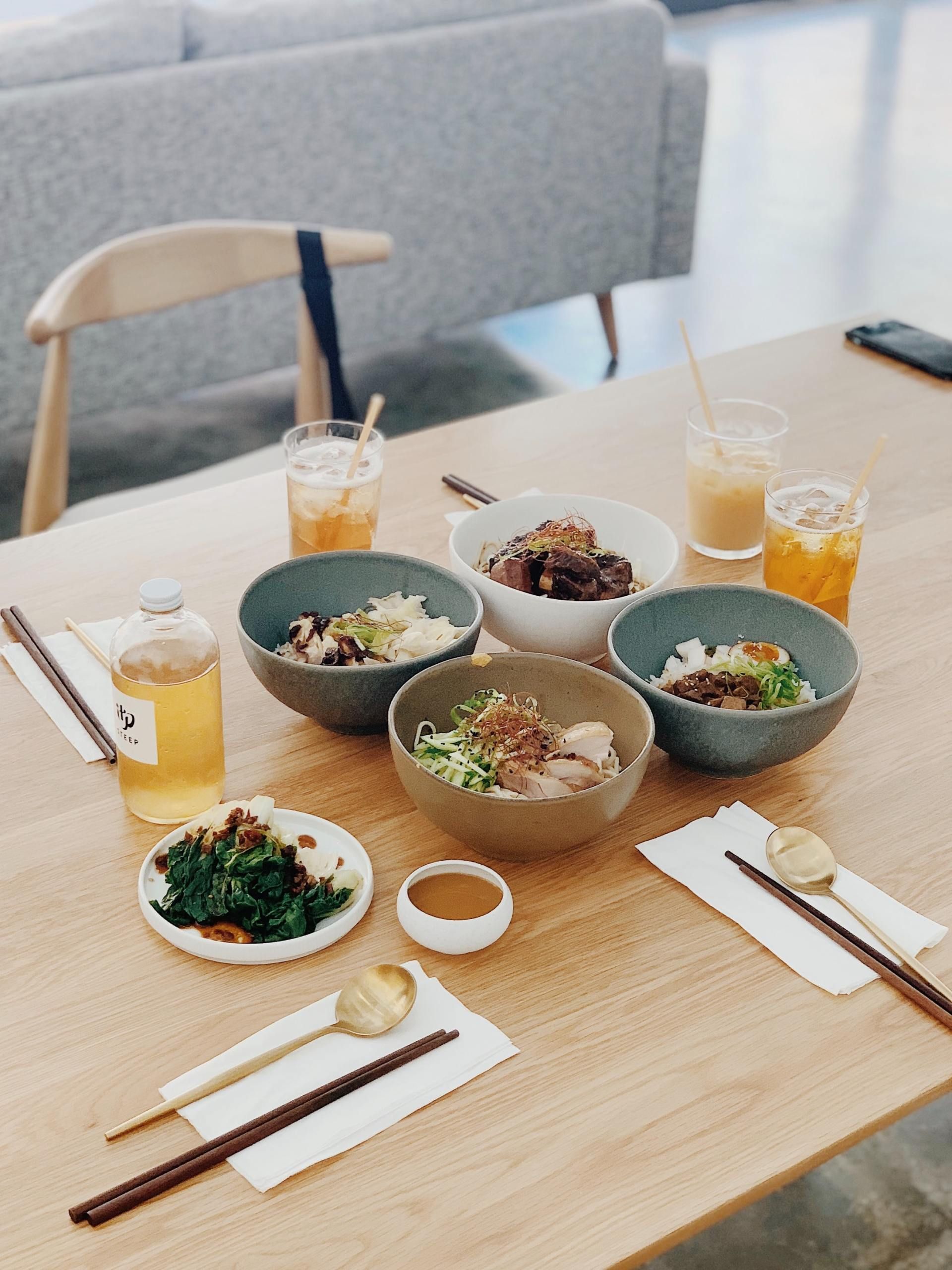Dining table with several bowls of food, drinks, chopsticks, and napkins in a bright cafe setting