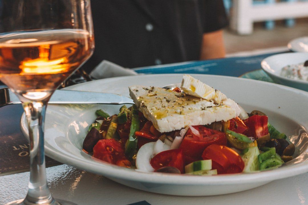 Salad with cherry tomatoes and feta on a white plate beside a glass of rosé at an outdoor table