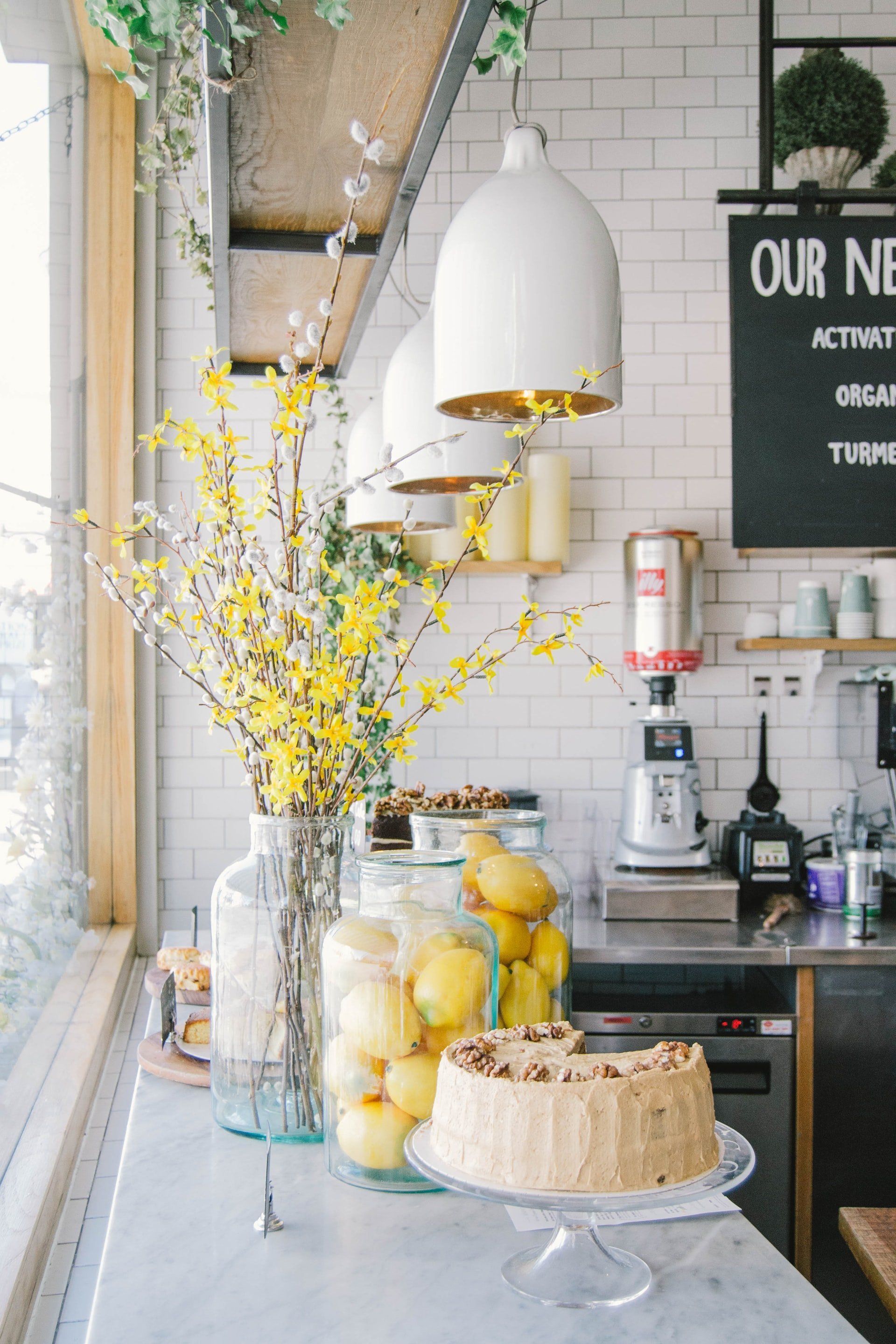 Bright kitchen counter with lemons in a vase, hanging white lamps, and a frosted cake on display