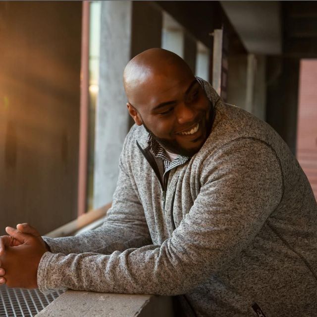 a man in a grey sweater leans on a railing and smiles -Fred Johnson Realtor