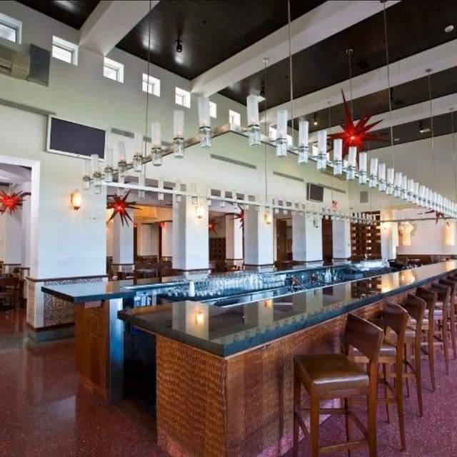 Modern bar interior with a long dark countertop, wooden stools, and hanging pendant lights