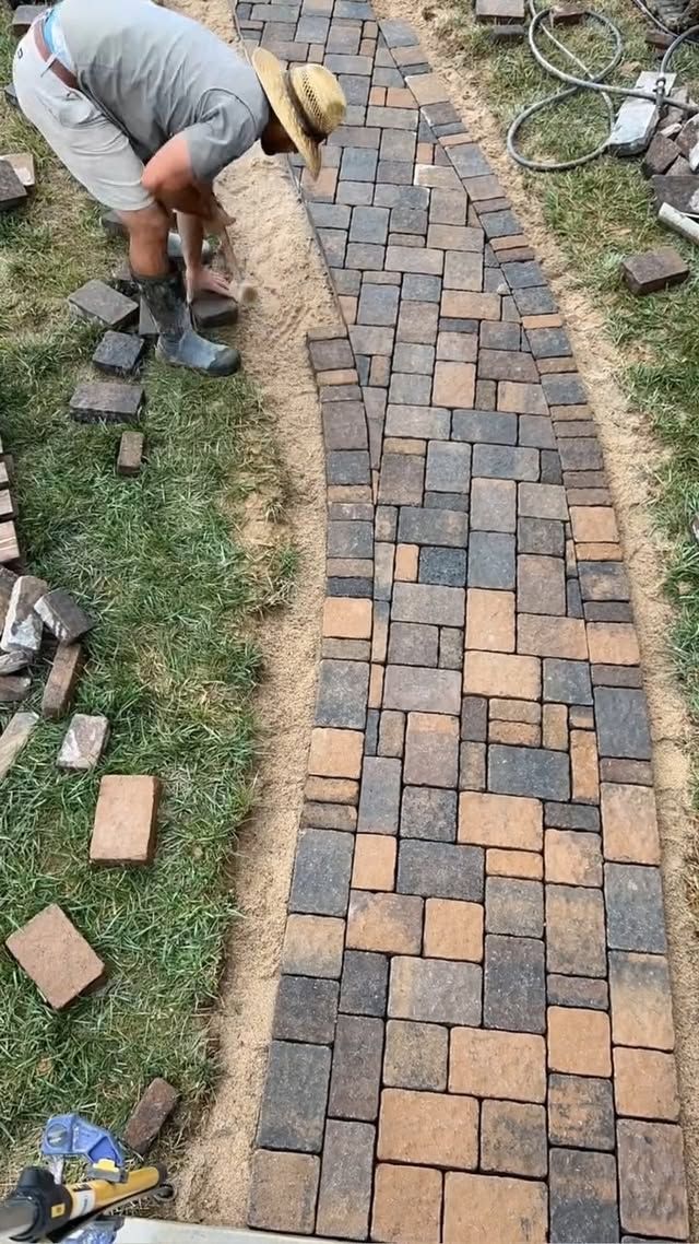 Person laying brick pavers for a narrow garden path outdoors