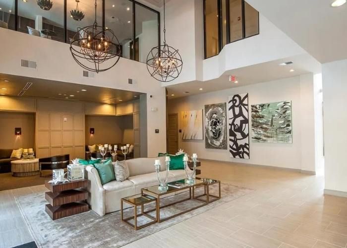 Spacious modern living room with white sofas, glass tables, high ceilings, and abstract wall art