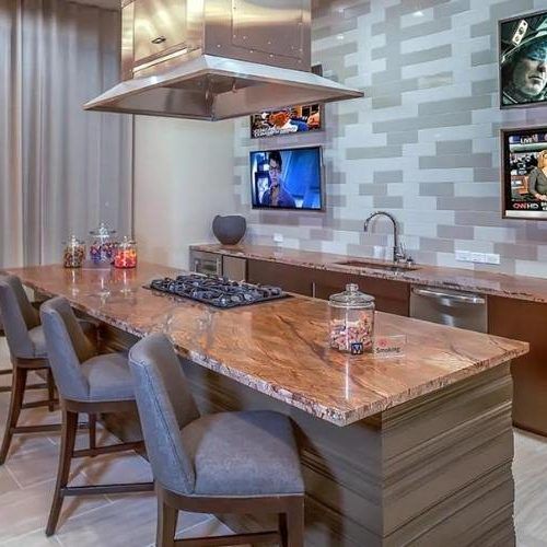 Modern kitchen with marble island, barstools, pendant hood, and wall-mounted TV.