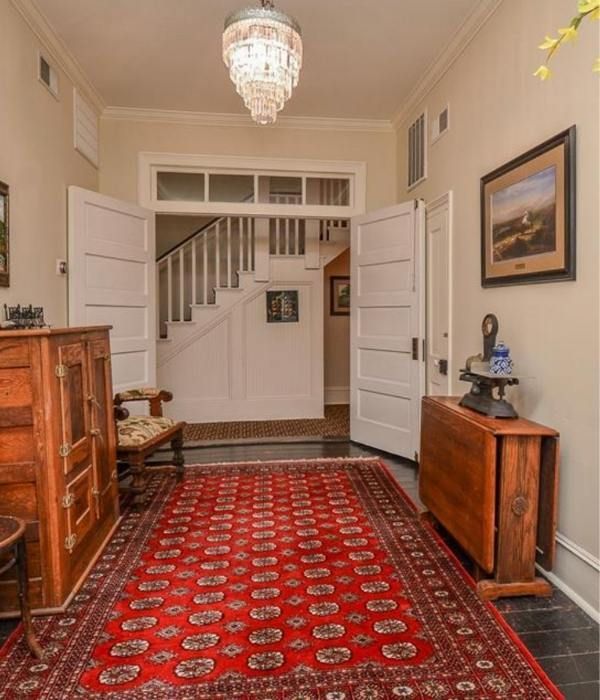 Elegant hallway with red patterned runner, white staircase, dark tile floor, and wooden furniture.