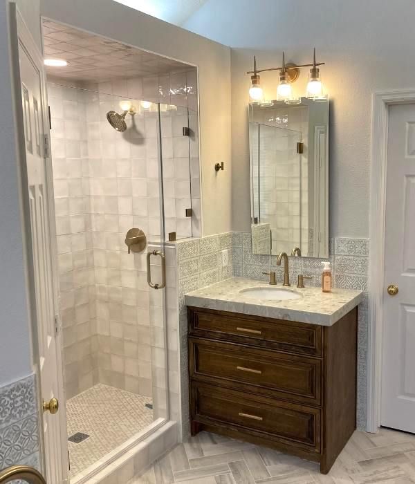 Modern bathroom with glass shower, marble vanity, mirror, and warm light fixtures.